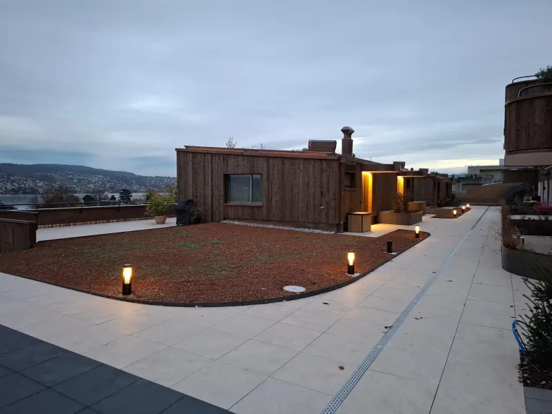 Terrasse mit Plattenweg, Pflanzfläche und Pollerleuchten in der Abenddämmerung